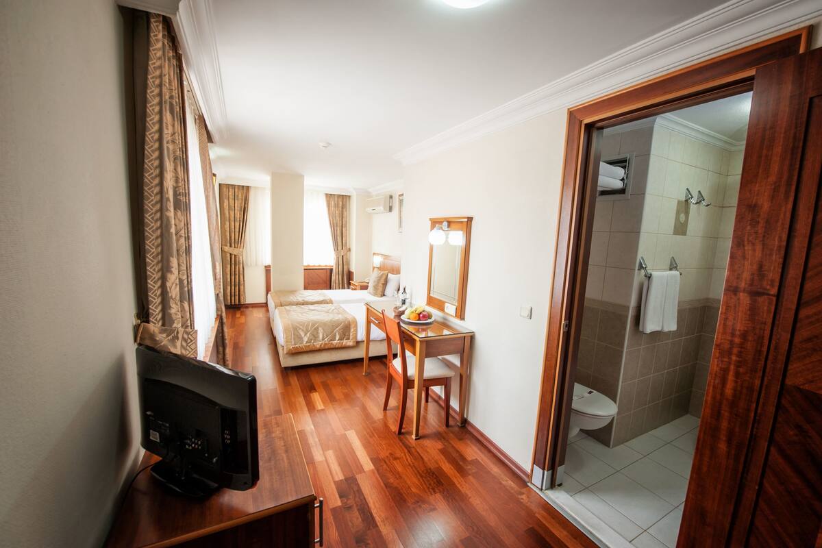 A hotel room with a bed, a desk with a chair, a television, and a bathroom with a shower and toilet.