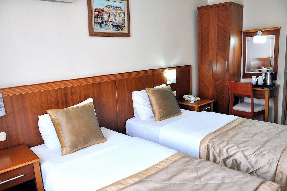 A hotel room with two beds, wooden headboards, a wooden wardrobe, a desk with a telephone, and a painting on the wall.