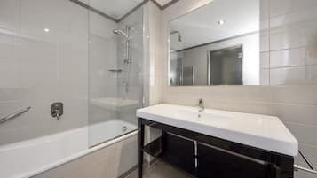 Un baño moderno con ducha envuelta en vidrio, una bañera blanca y un tocador negro con espejo.