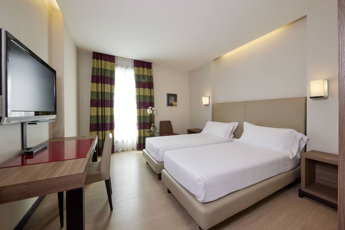 Ein Hotelzimmer mit zwei Betten, einem Fernseher, einem Schreibtisch und einem Sessel.