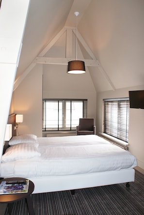 Una habitación de hotel moderna con una cama grande, una silla y una mesa. Hay ventanas con persianas, una lámpara y una luz en el techo.