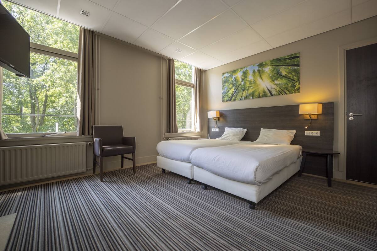 Une chambre d’hôtel avec un grand lit, une chaise, un bureau et une fenêtre donnant sur les arbres.