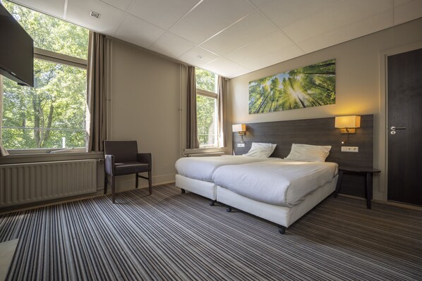 Habitación de hotel con una cama grande, una silla, un escritorio y una ventana con vista a árboles.