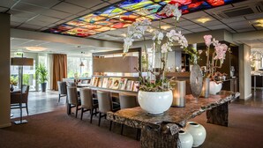 Un espace d’accueil doté d’un grand comptoir en bois, de vases blancs et d’orchidées. On y trouve également un plafond en vitrail et, au fond, un bar.