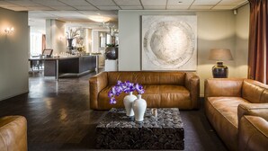 Un hall d’entrée avec des canapés en cuir, une table basse ornée de vases et un grand tableau abstrait accroché au mur.