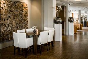 Un coin repas agrémenté d’un mur en pierre, de chaises blanches, d’une table en bois et de grands vases remplis de fleurs.
