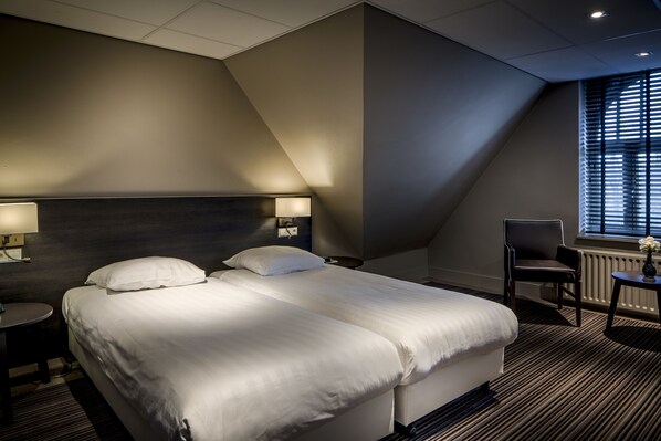 A hotel room with a large bed, two bedside tables with lamps, a chair, and a window with blinds.