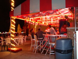 An outdoor dining area with tables and chairs, a trash bin, and a building with red and white striped awning.
