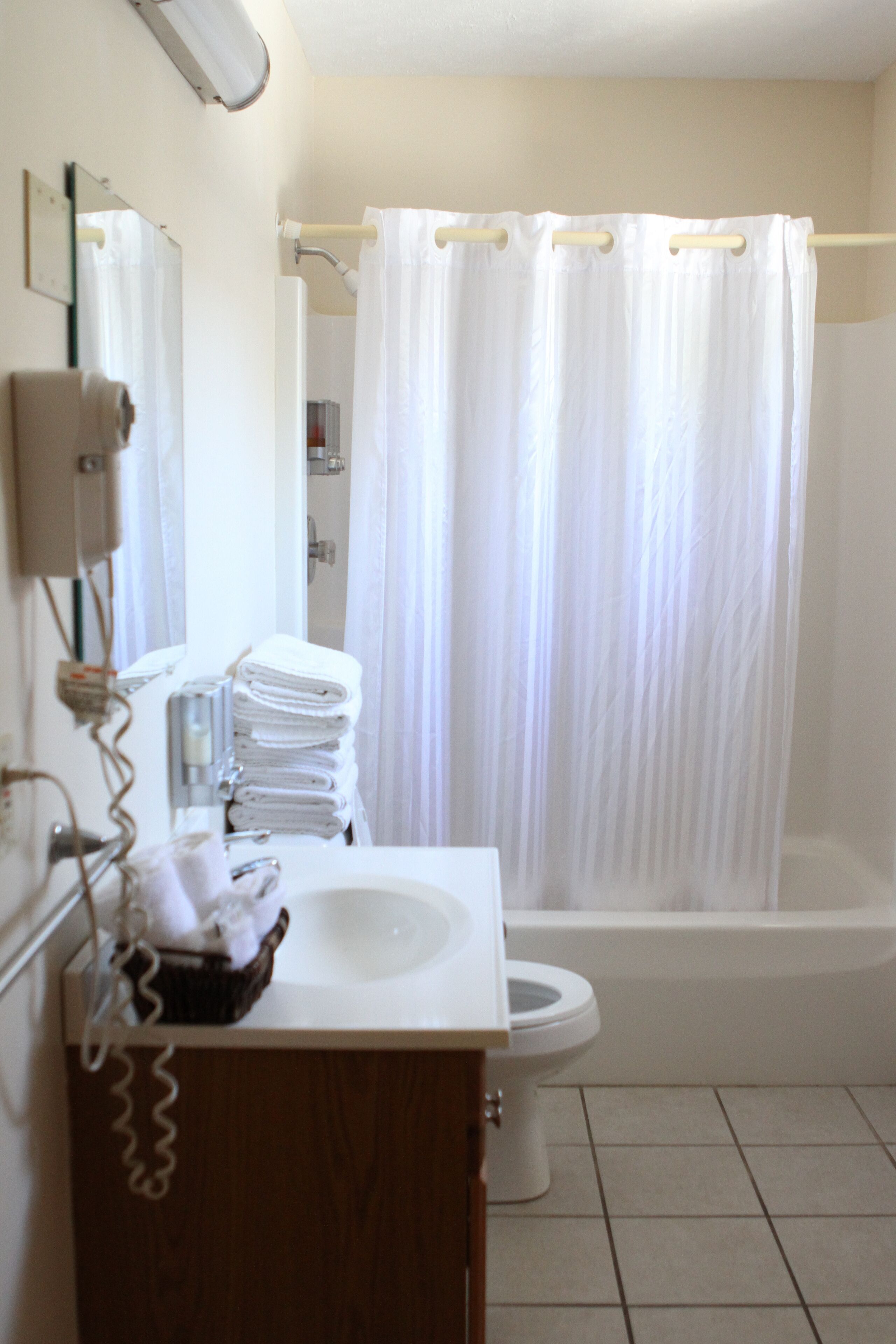A bathroom with a white sink, toilet, and bathtub. There is a stack of white towels on the counter, and a shower curtain is hanging over the bathtub.