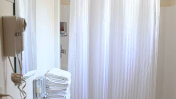 A bathroom with a white sink, toilet, and bathtub. There is a stack of white towels on the counter, and a shower curtain is hanging over the bathtub.