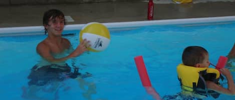 A swimming pool with a person and a child holding a ball.