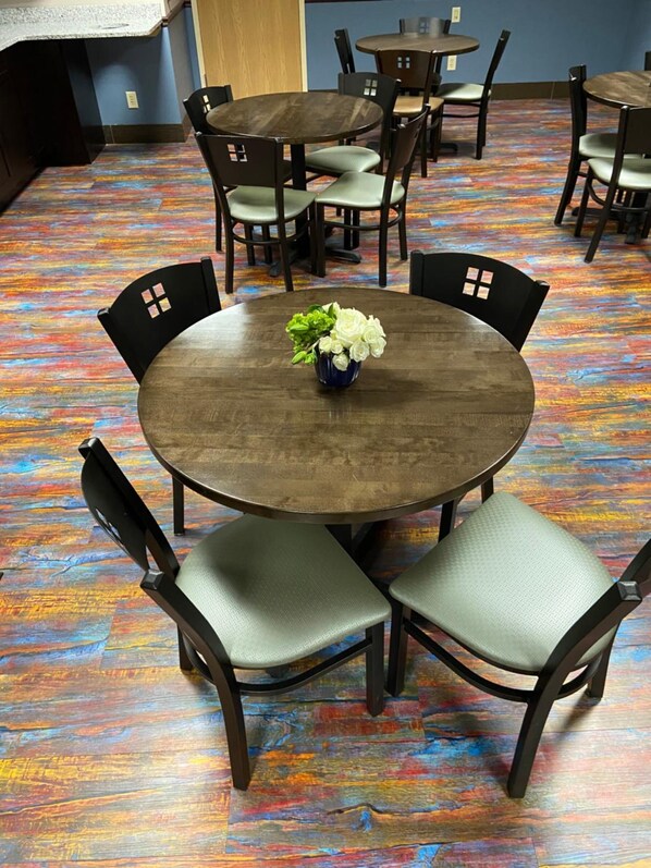 A room with a round table and four chairs, a vase with flowers, and a colorful wooden floor.
