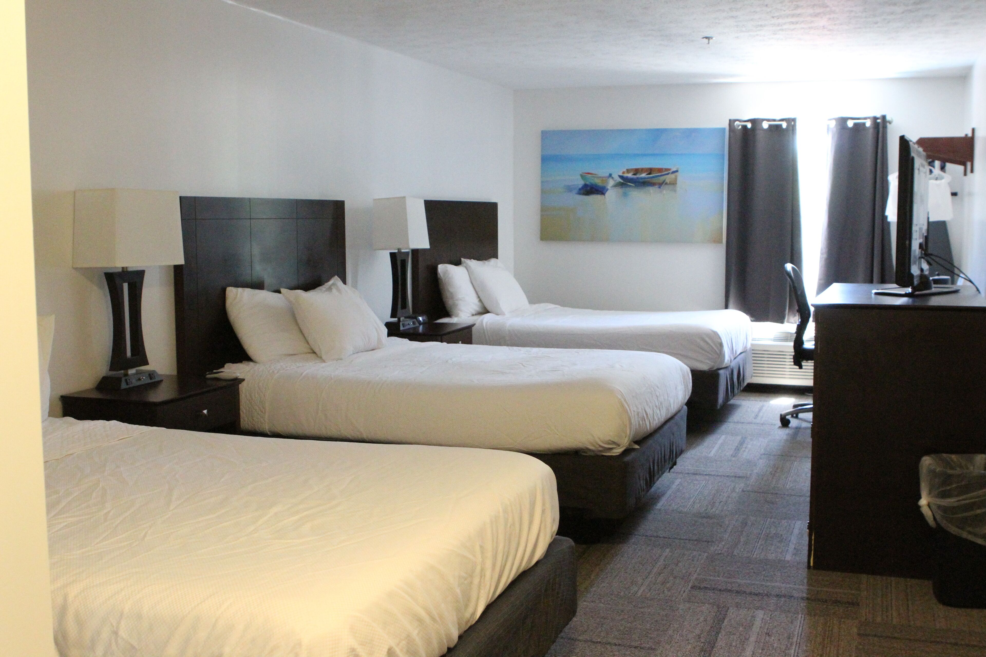 A hotel room with three beds, a desk, and a painting of a beach scene.