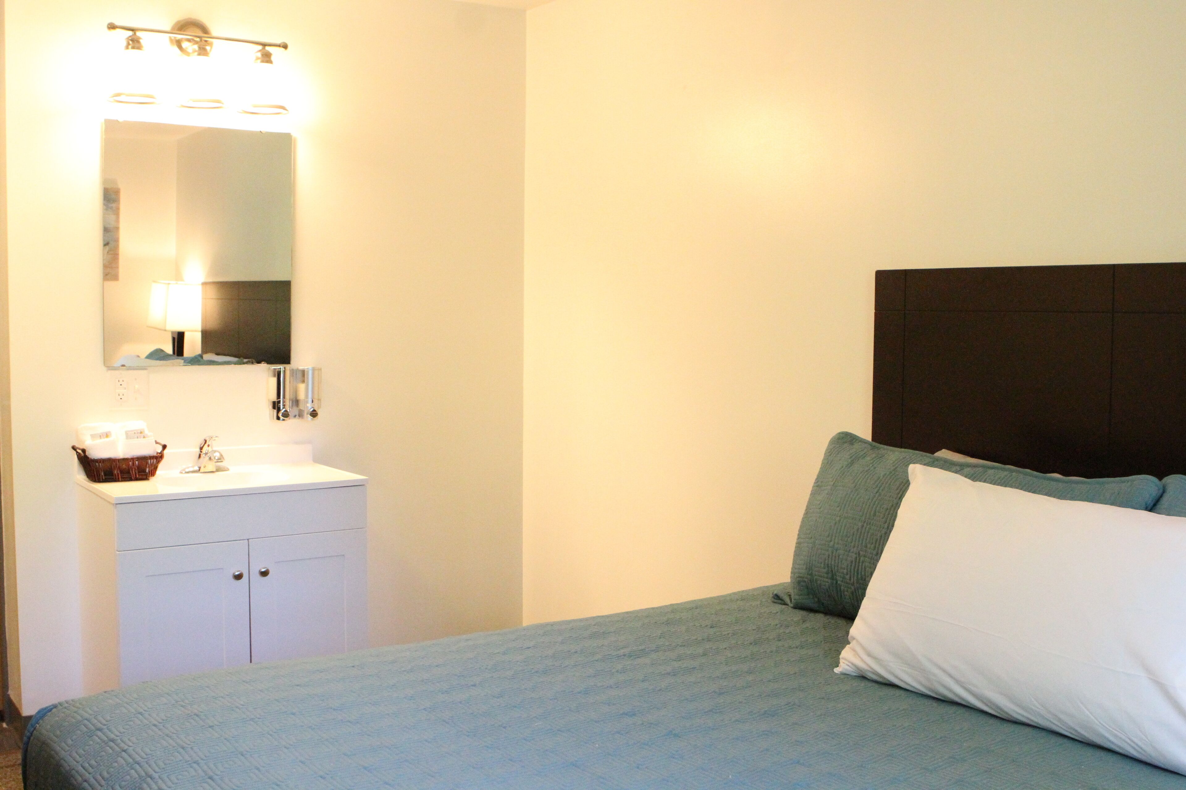 A bedroom with a bed, a nightstand, a mirror, and a wall-mounted light fixture.