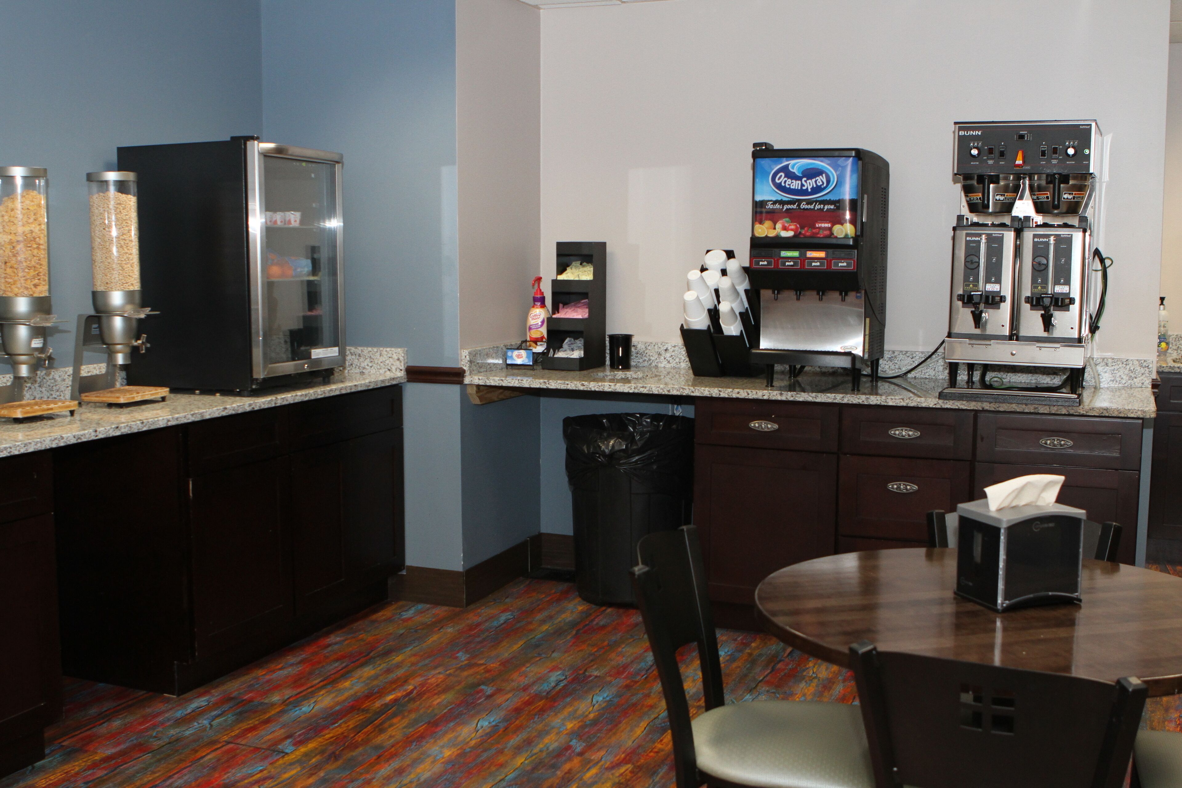 A hotel bar with a coffee machine, a bottle of hand sanitizer, and a trash can.