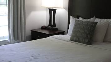 A neatly made bed with white linens, a bedside table with a lamp, and a window with curtains.