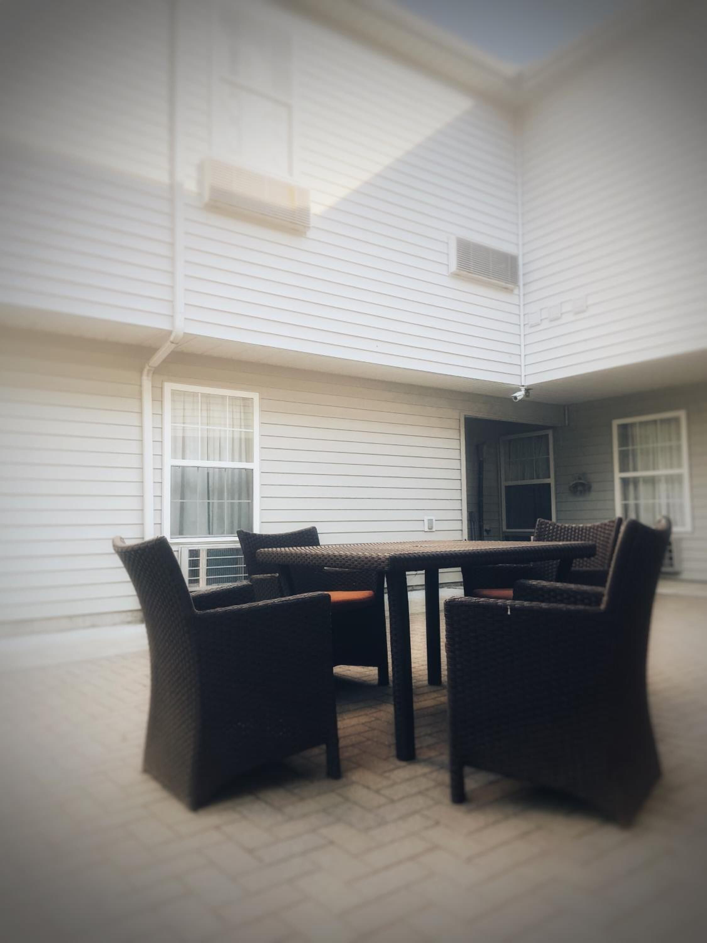 A covered patio with a round table and chairs, a door, and a window.