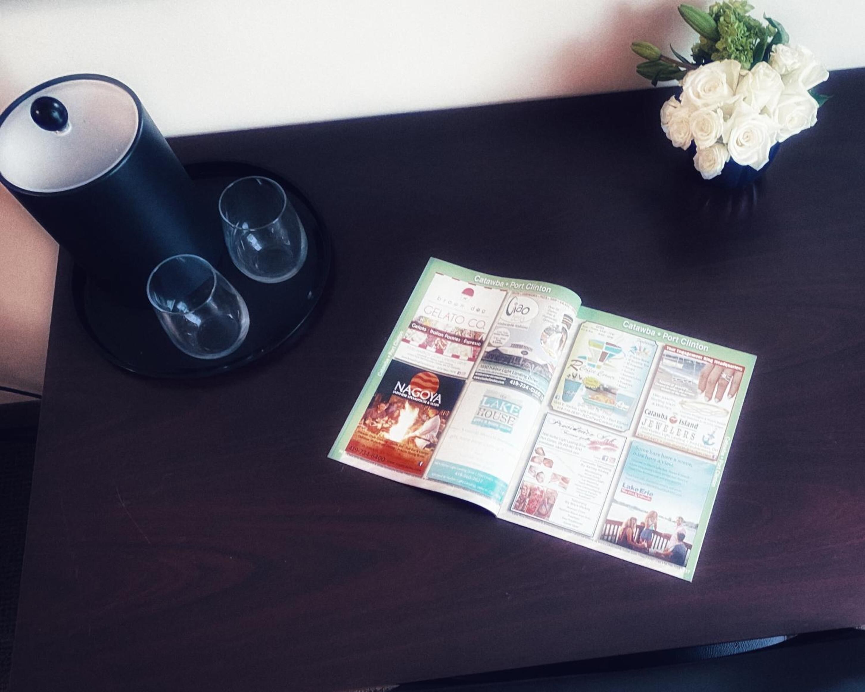 A brochure on a dark wooden table with a black lamp and a vase of white flowers.