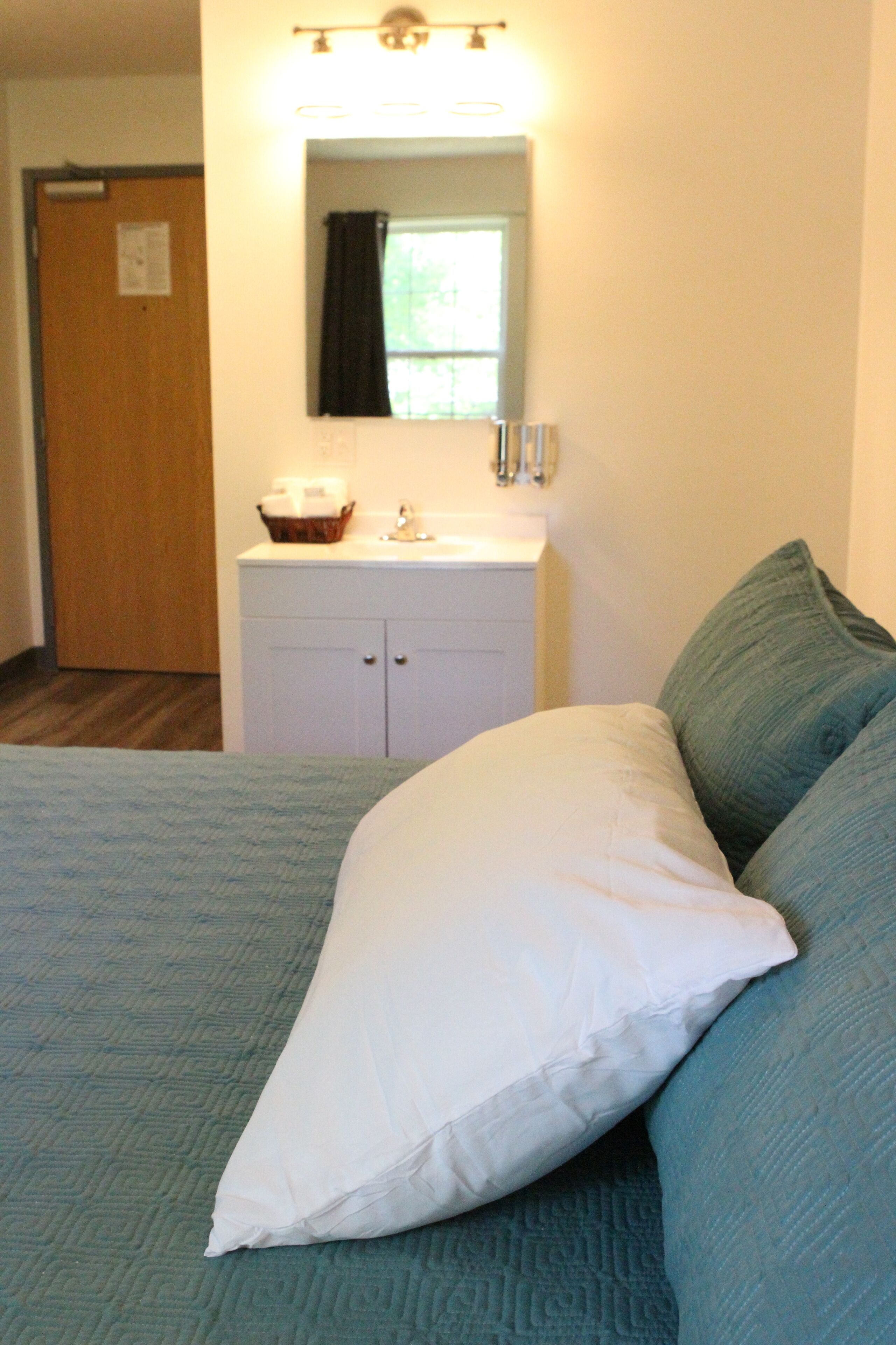 A bedroom with a bed, a nightstand, a mirror, a window, and a door.