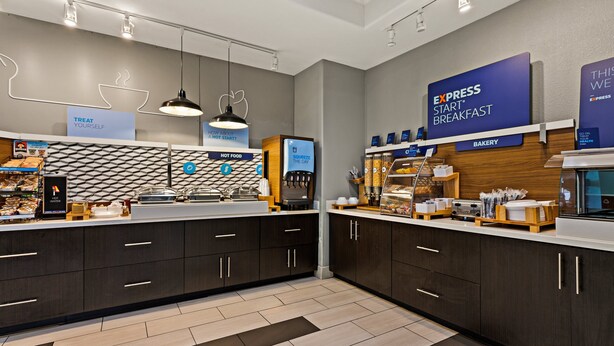 Un espace moderne dédié au petit-déjeuner, avec un panneau indiquant « PETIT-DÉJEUNER EXPRESS », un coin « PLAT CHAUD » et un espace « BOULANGERIE ».