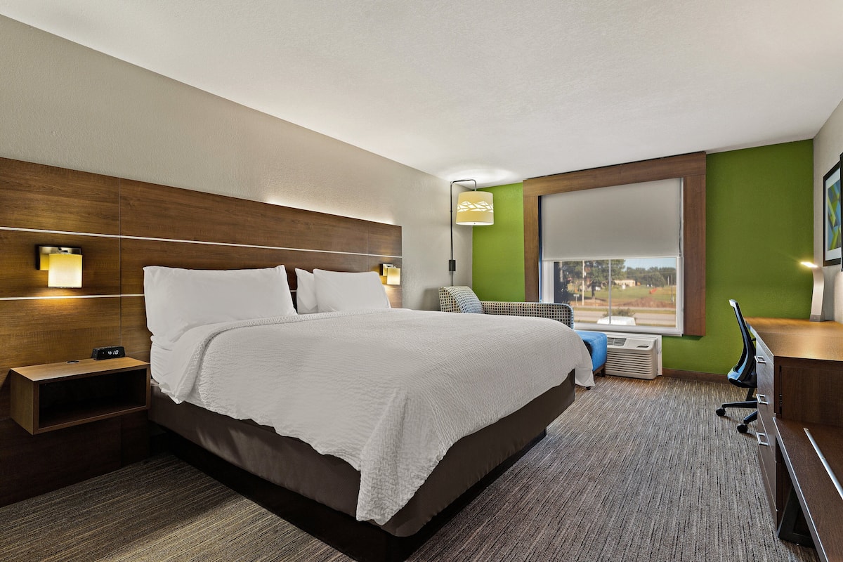 A hotel room with a large bed, a desk, a chair, a window, and a view of the outdoors.