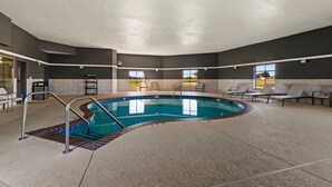 Une piscine intérieure au design incurvé, entourée de chaises longues et dotée d’un sol carrelé.