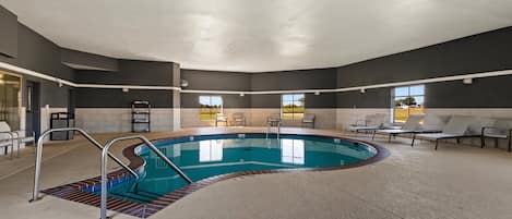 An indoor swimming pool with a curved design, surrounded by lounge chairs and a tiled floor.