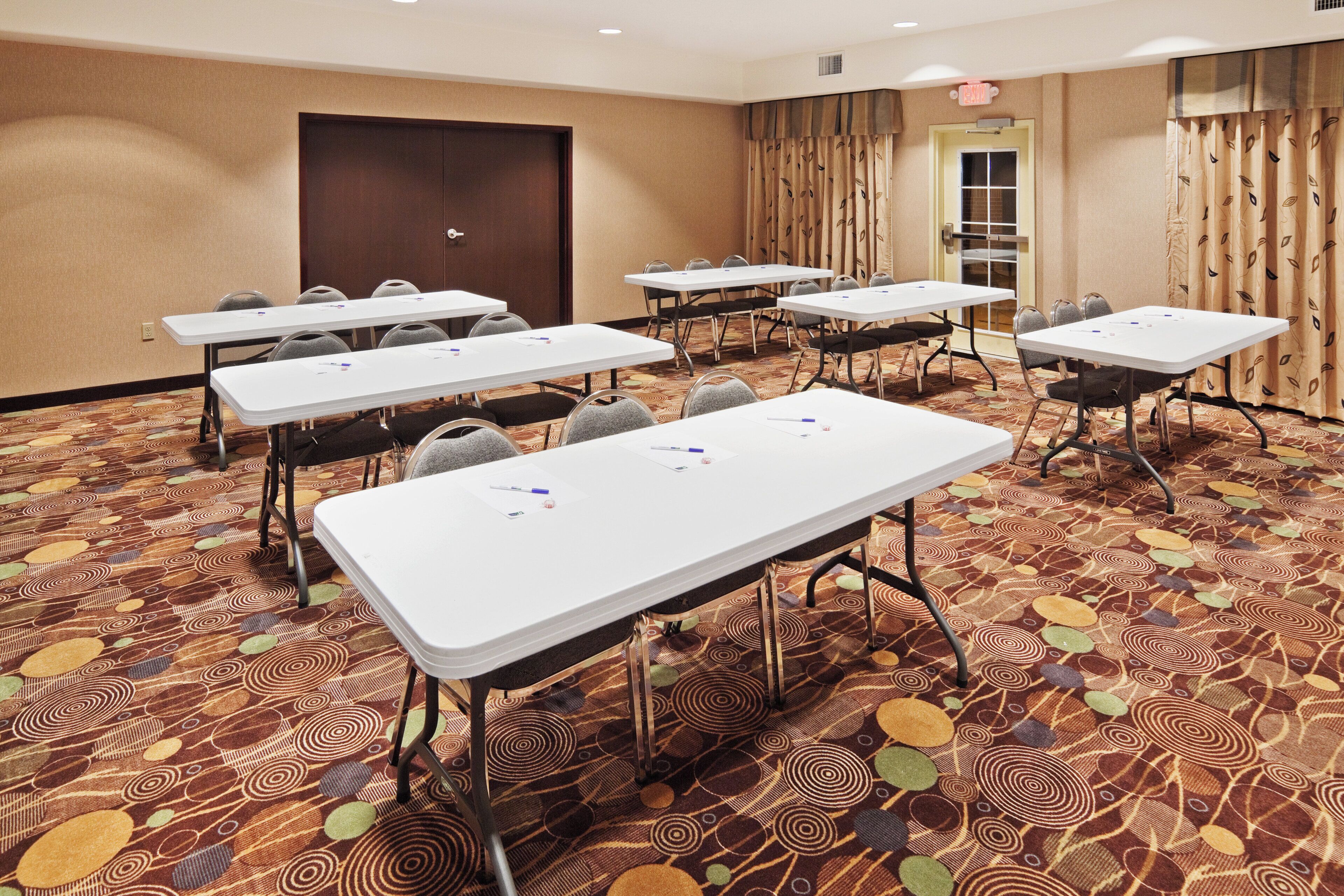 A conference room with multiple tables and chairs, carpeted floor, and a door in the background.