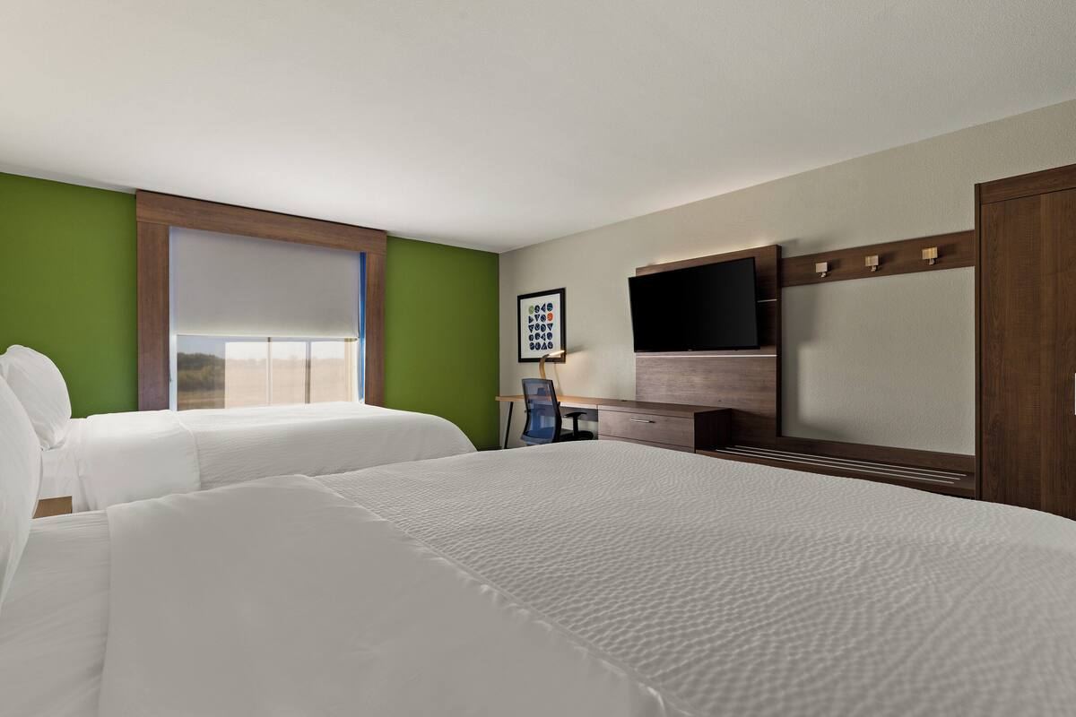 A hotel room with two beds, a desk, a chair, a TV, and a window with blinds.