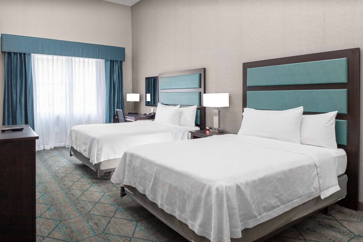 Habitación de hotel con dos camas, un escritorio y una ventana con cortinas.