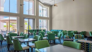 Een ruime, overdekte eetruimte met hoge plafonds, grote ramen en groene beklede stoelen.