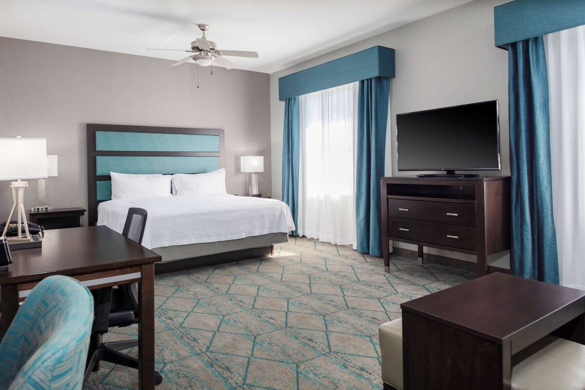 Una habitación de hotel con cama, escritorio, silla, televisor y ventilador de techo.