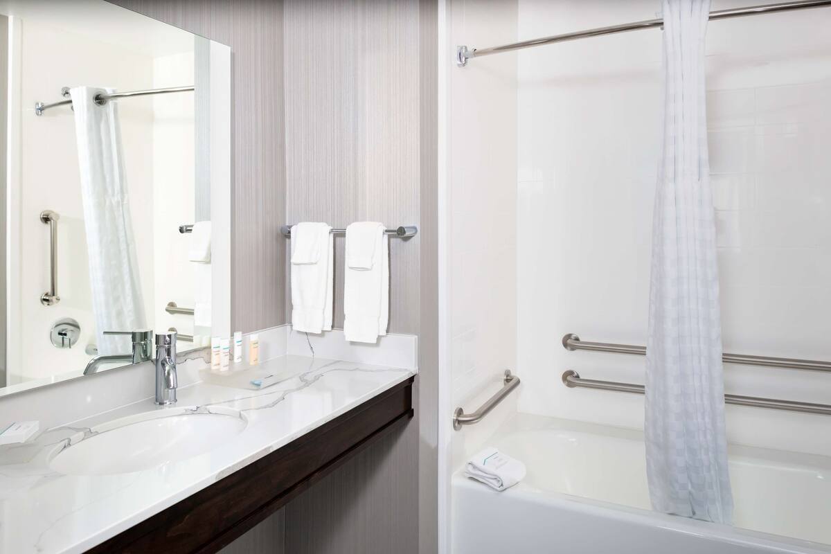Un baño con lavamanos blanco, espejo y zona de ducha.