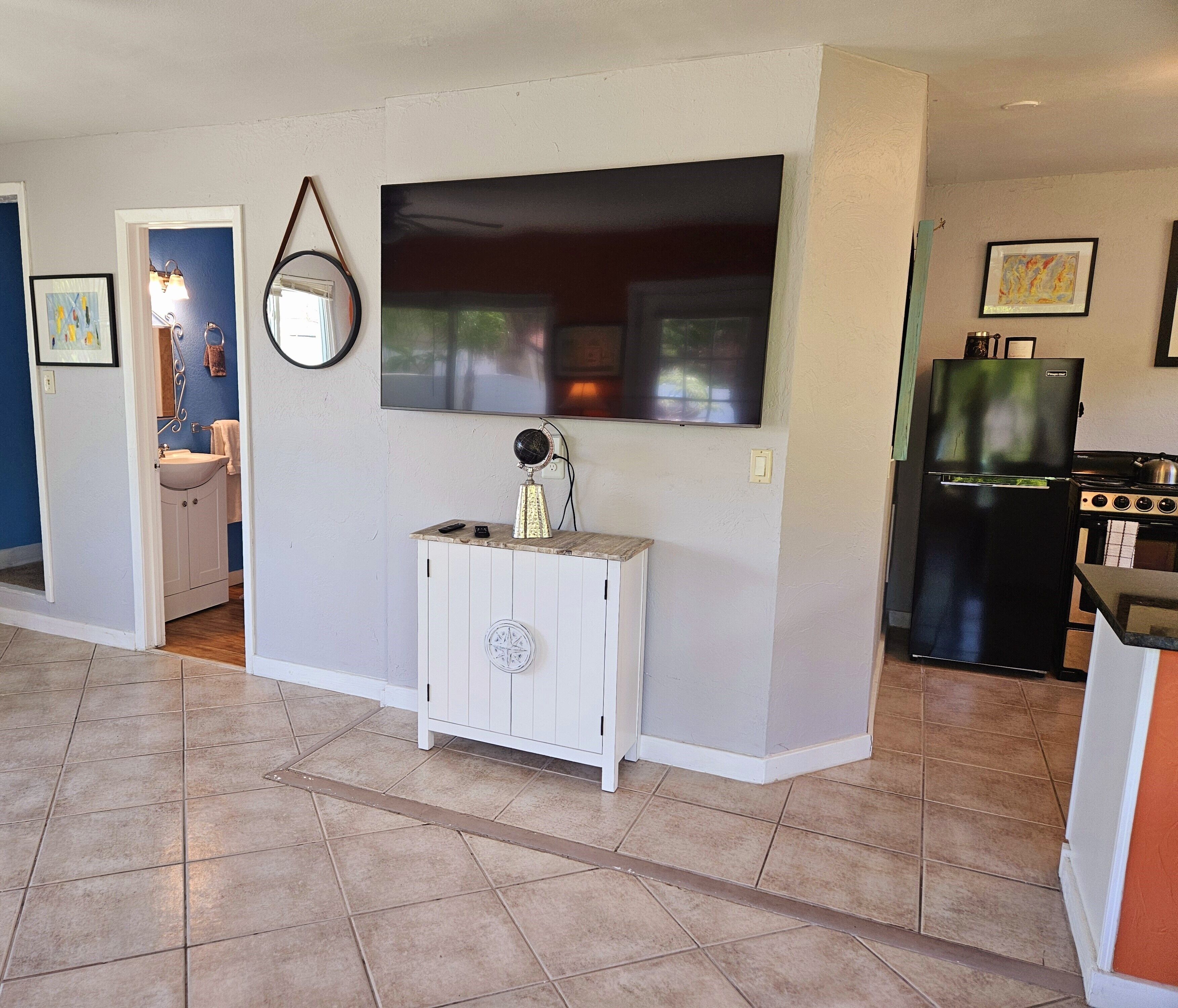 A kitchen with a large TV, a white cabinet, and a black refrigerator.