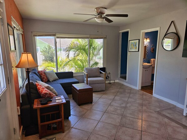 A living room with a sofa, armchair, and coffee table, a ceiling fan, and a view of the outdoors.