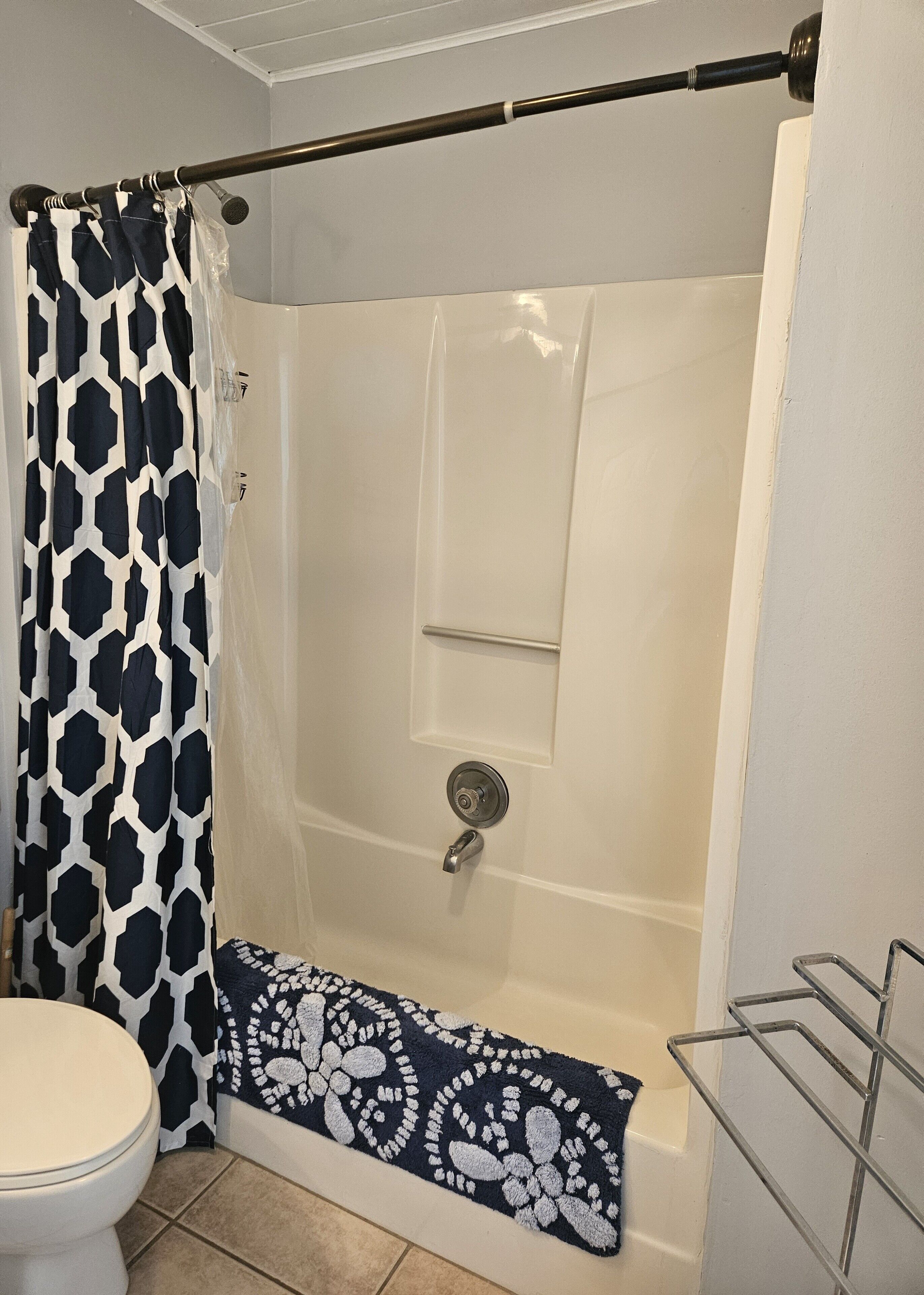 A shower area with a white shower curtain, a shower control panel, and a metal towel rack.