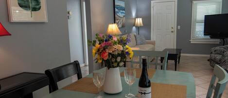 Un coin repas avec une table dressée pour deux personnes, un vase de fleurs et une bouteille de vin.