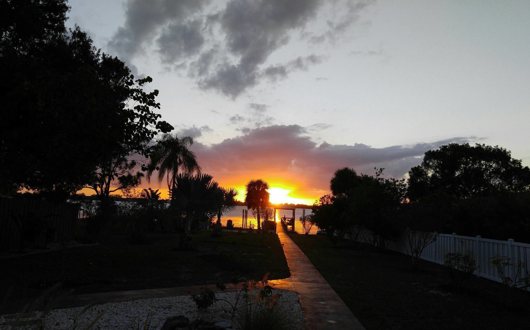 A sunset view with a pathway leading to a gazebo, surrounded by trees and a fence.