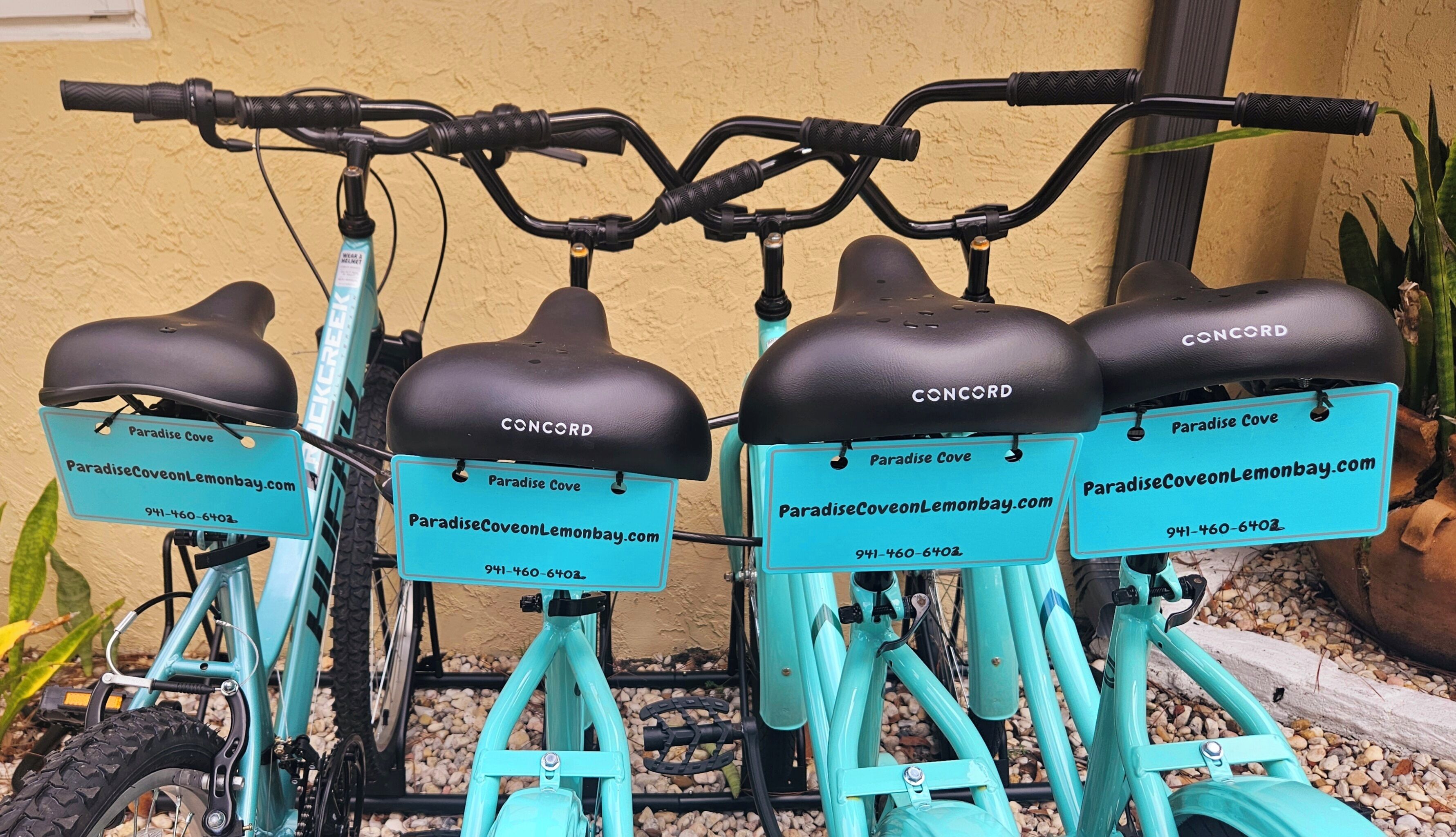 Cuatro bicicletas tándem con asientos negros y estructuras turquesa, cada una con una etiqueta azul que muestra 'Paradise Cove' y una dirección web.