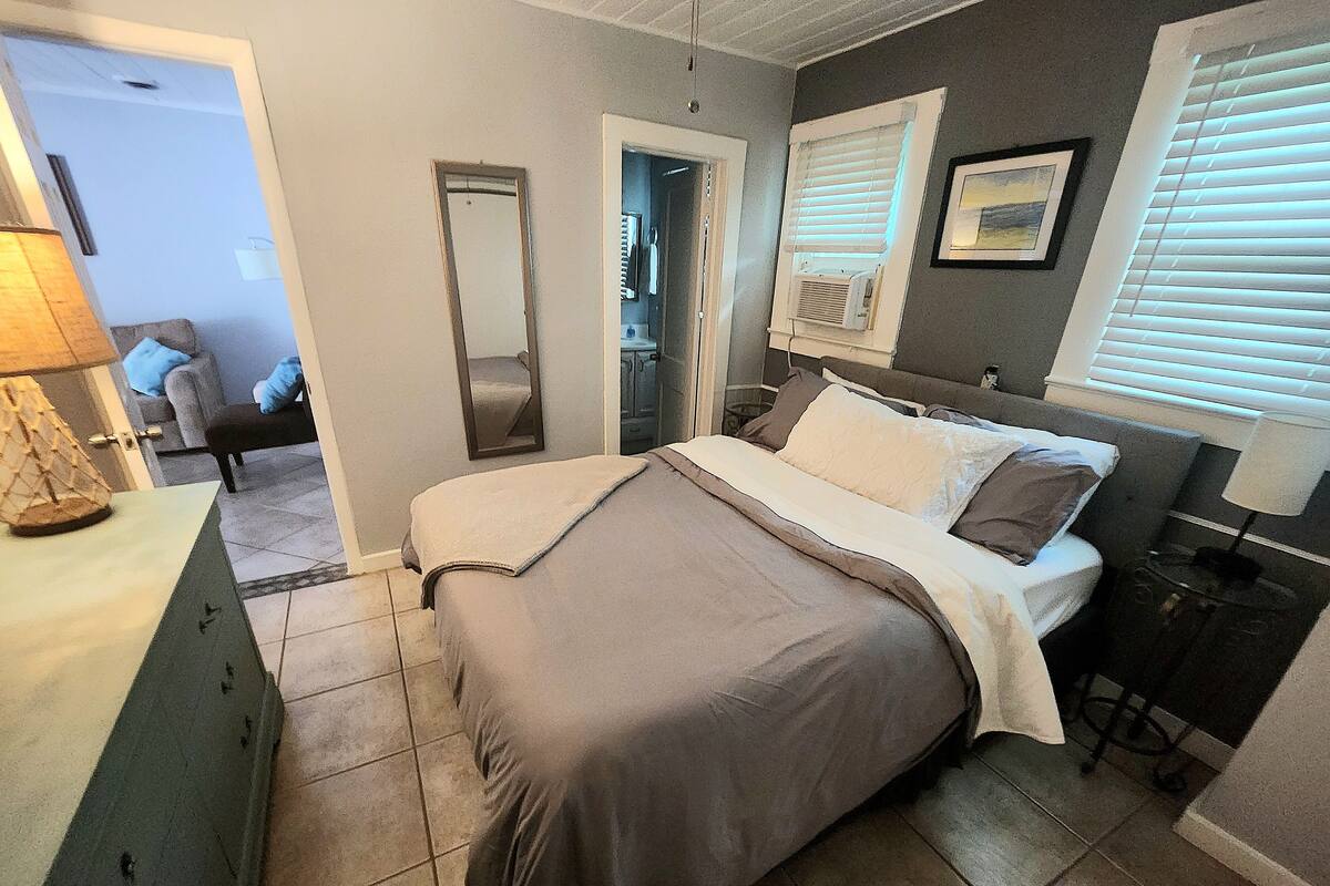 Ein Schlafzimmer mit einem Bett, einem Schminktisch, einem Spiegel und einem Fenster mit Jalousien.