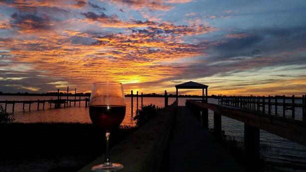 Vista do pôr do sol com um copo de vinho tinto em um cais.