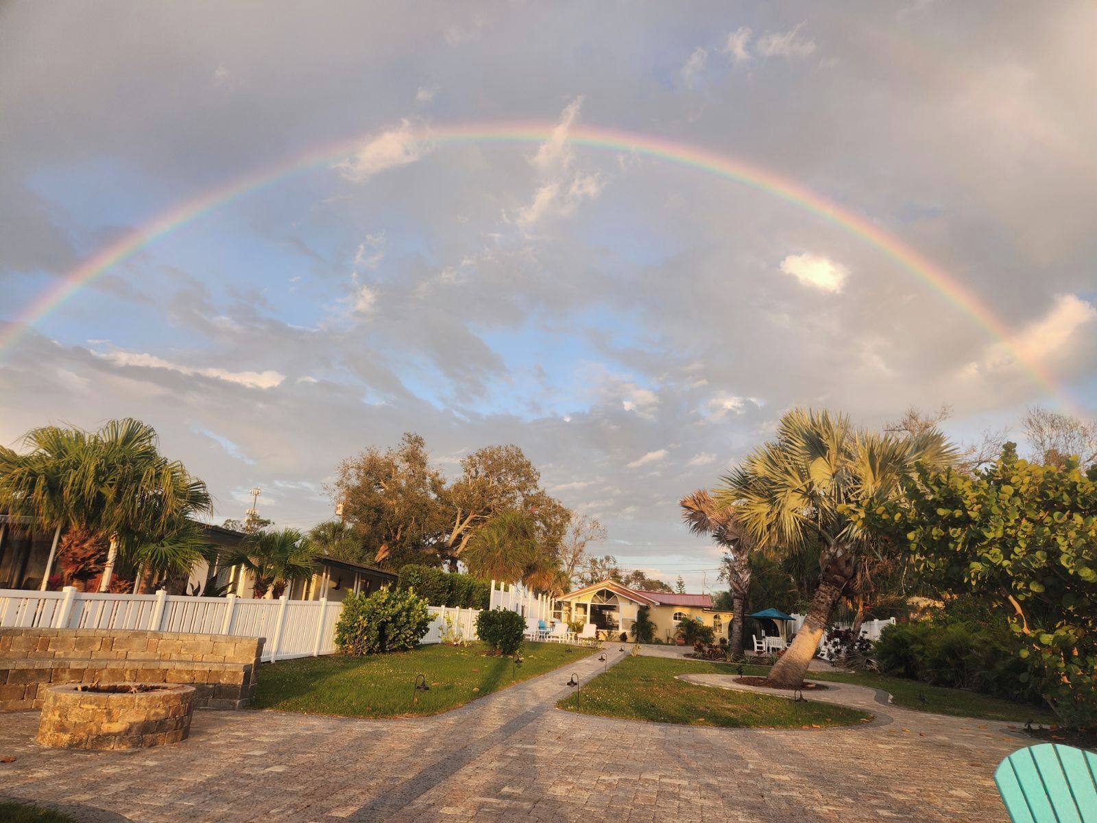 Un sendero pavimentado que lleva a una casa con cerca blanca y una fogata.