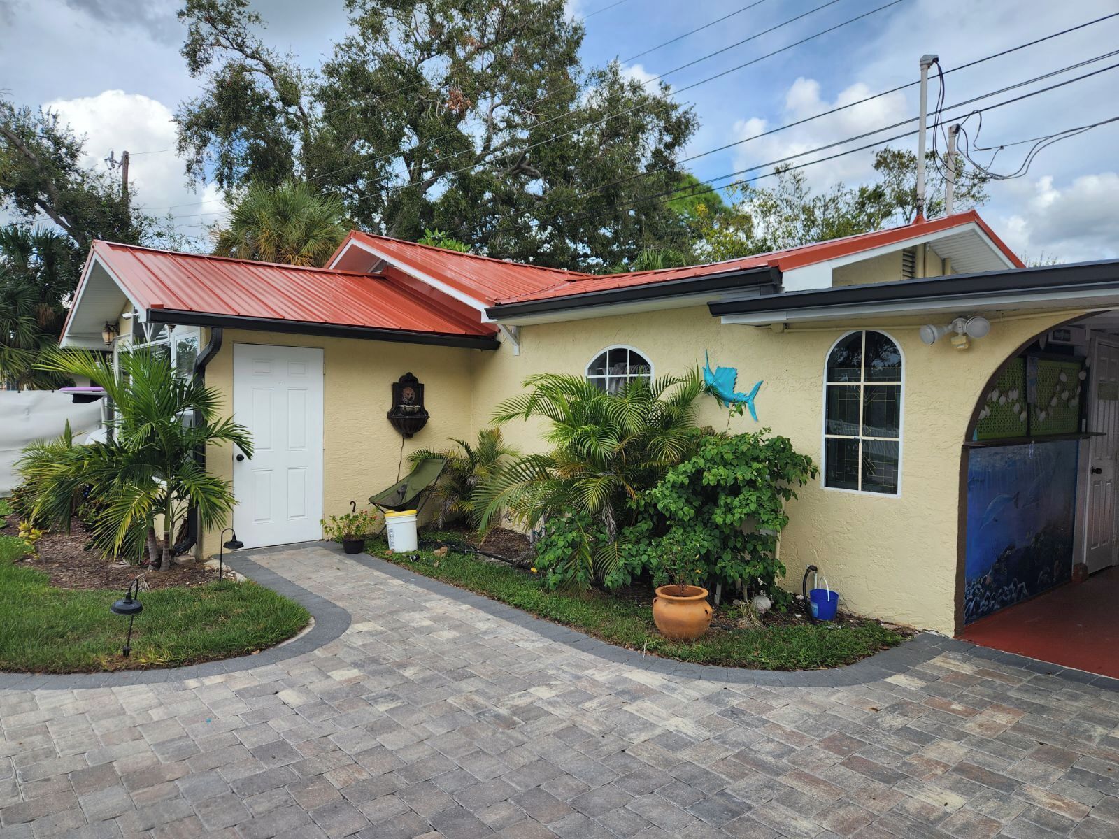 A house with a red roof, a front porch, and a garden with various plants and a large pot.