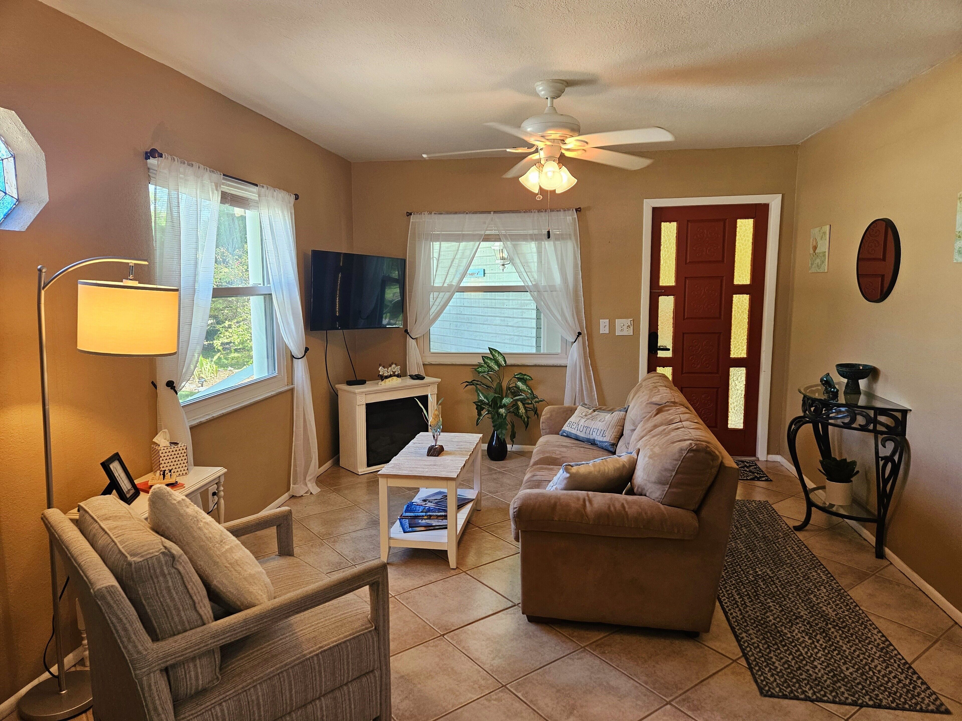 A living room with a sofa, armchair, TV, fireplace, and a ceiling fan.