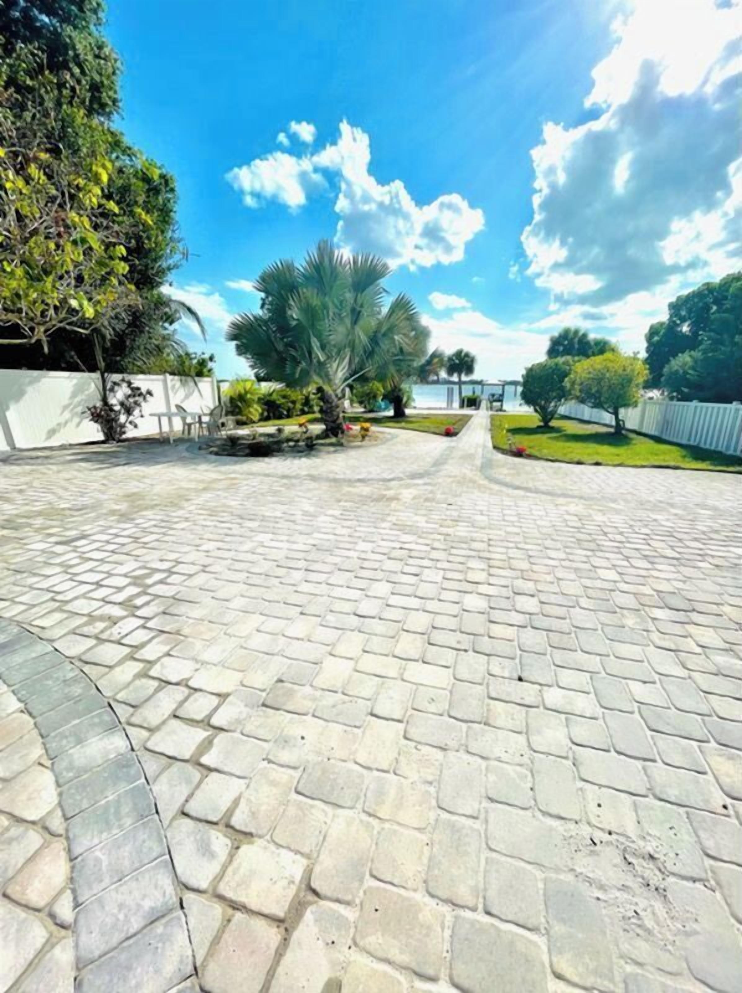 A paved courtyard with a palm tree, a white fence, and a clear blue sky.