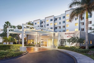 Una entrada de hotel moderna con un corredor cubierto, palmeras y un letrero que dice 'Residence Inn Marriott'.