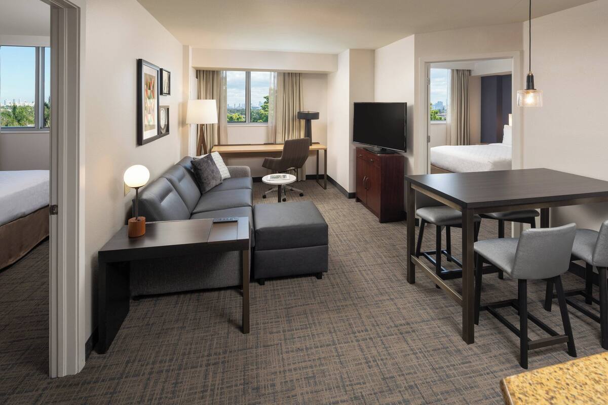 A hotel room with a sofa, a desk, a television, and a dining area.