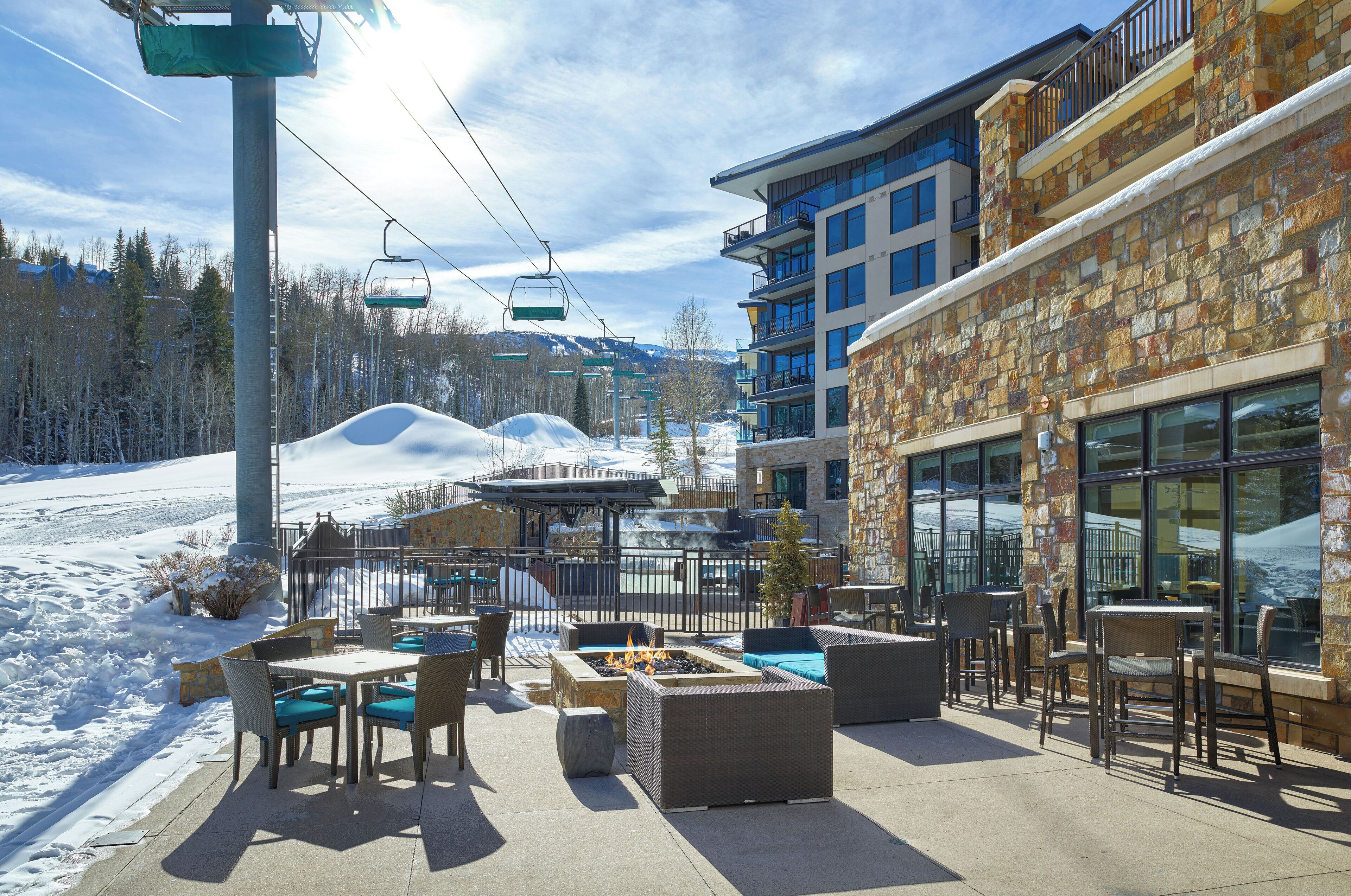 An outdoor patio with seating and a fire pit, overlooking a snowy mountain landscape.