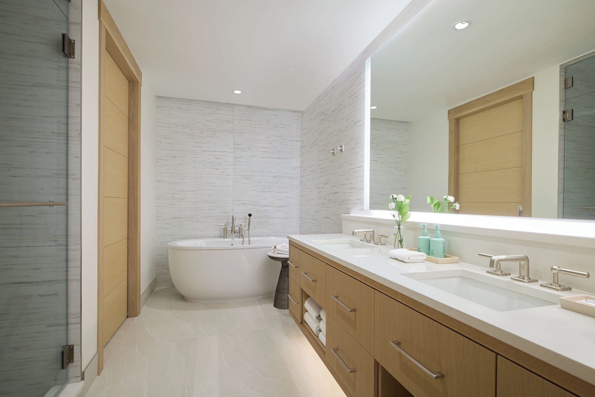 A modern bathroom with a bathtub, two sinks, and a large mirror.