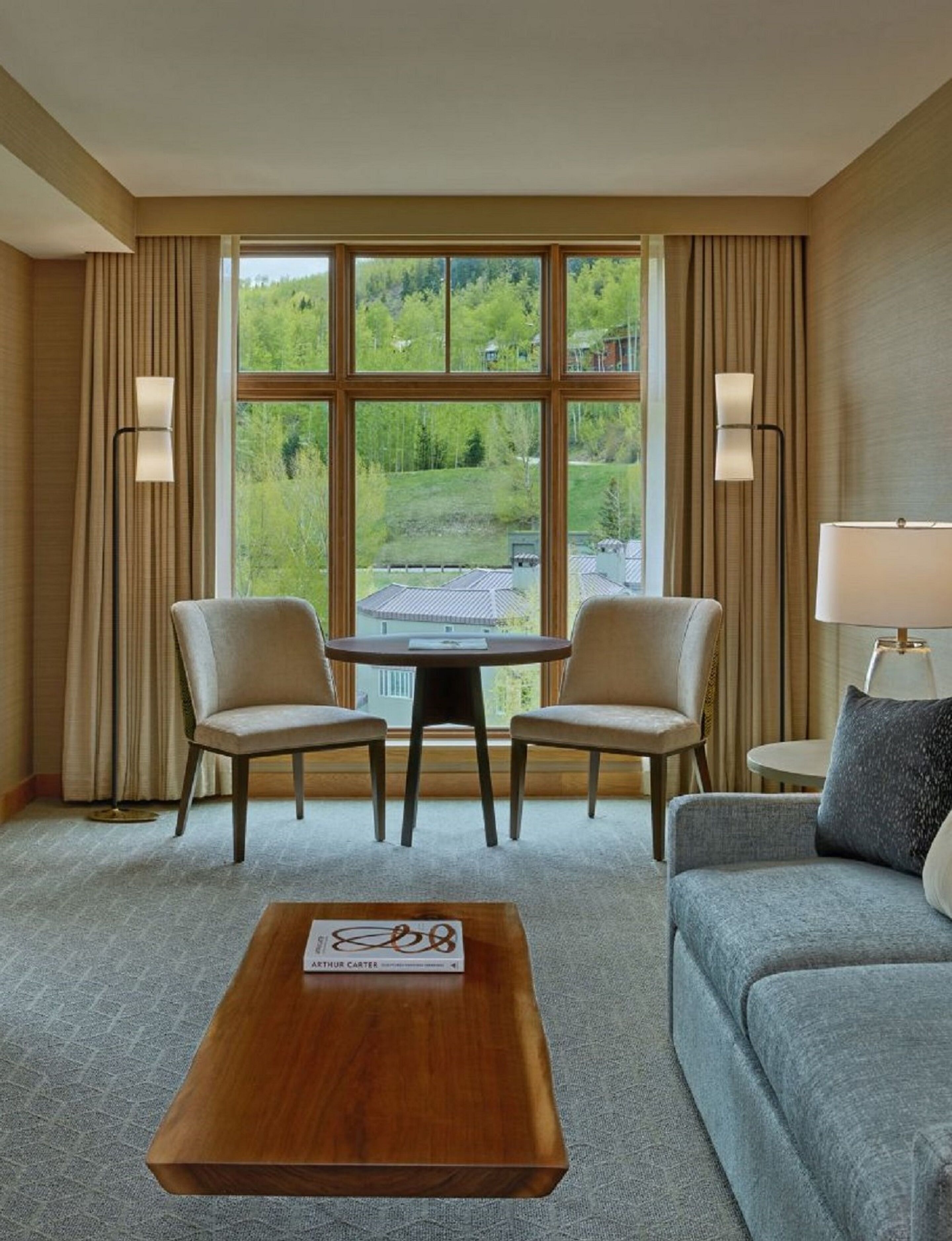 Habitación de hotel con un ventanal grande, dos sillones, una mesa redonda, un sofá y una lámpara.